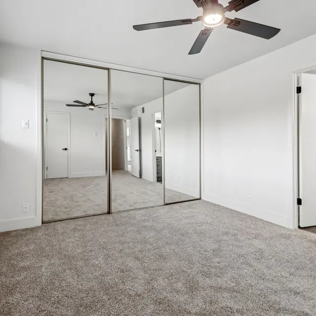 Modern Bedroom Interior A modern bedroom featuring a light-colored wall and carpet, with a ceiling fan and large mirrored closet doors.