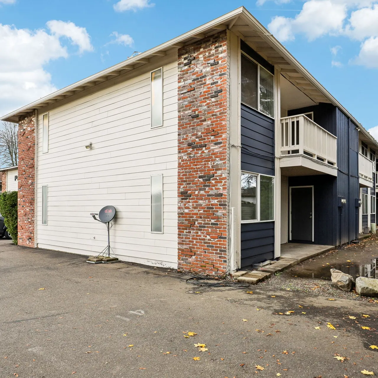 Exterior view of a two-story apartment complex with a mix of brick and siding, surrounded by a parking lot and greenery.