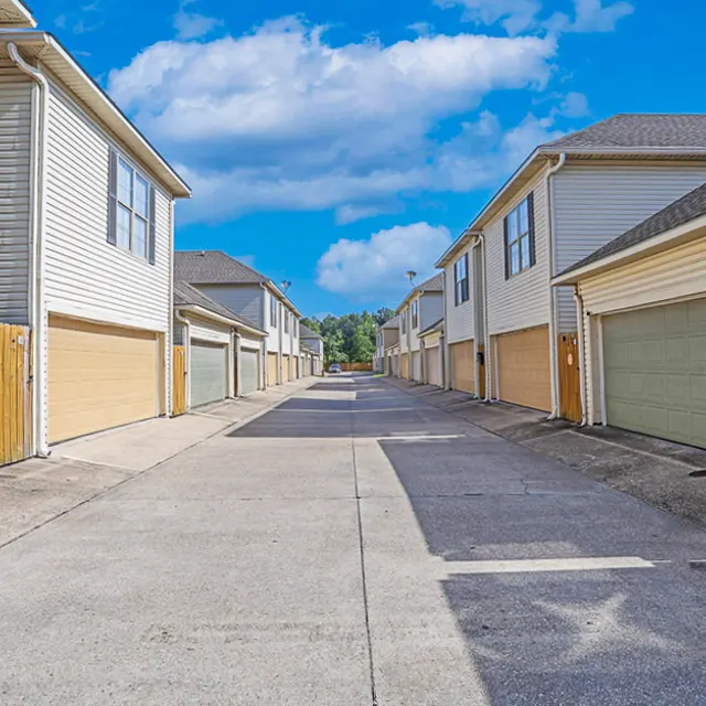 A quiet residential alley flanked by buildings with beige siding and garages.