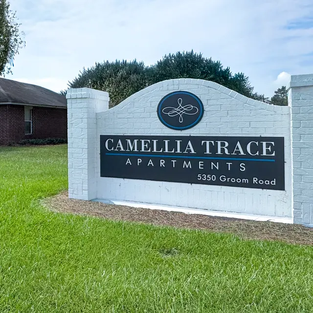 Sign for Camellia Trace Apartments located on Groom Road, featuring a blue logo and white brick structure.