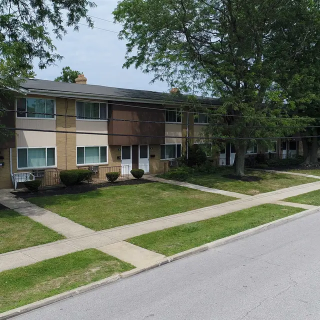 View of an apartment complex with two-story buildings surrounded by grass and trees.