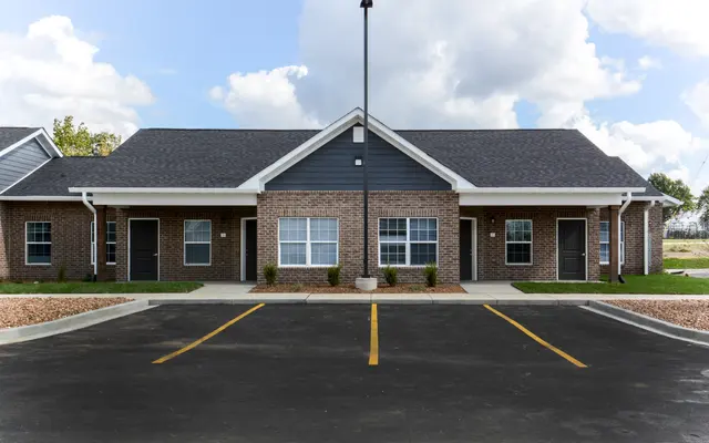 A modern apartment complex featuring brick and siding exteriors, with a blacktop parking lot and landscaped areas