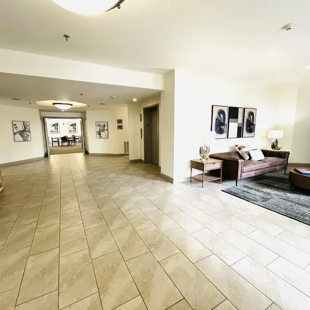 Modern Lobby Area A spacious lobby area featuring a tiled floor, a couch, and an armchair. Decorative art pieces hang on the walls and a plant is located next to the seating area.