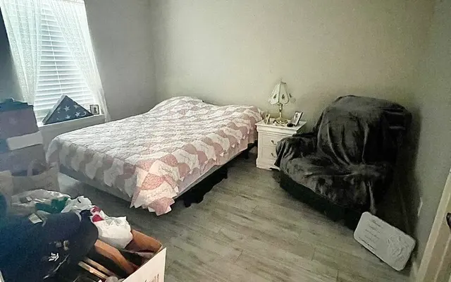 A tidy bedroom with a bed covered in a patterned blanket, a chair in the corner, and a window allowing natural light.