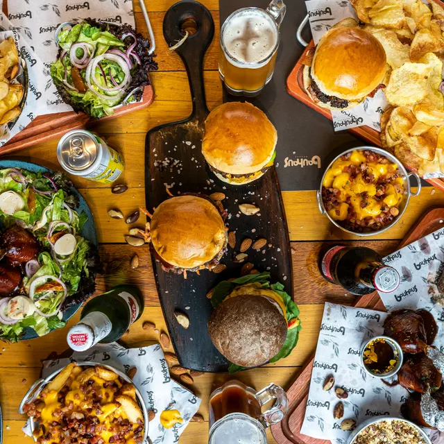 Finn Hall An overhead view of a table filled with a variety of foods including burgers, salads, and chips, accompanied by drinks and sauces, presented on trays and in bowls.