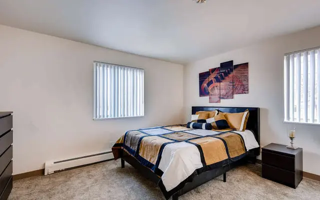 A modern bedroom featuring a bed with patterned bedding, bedside tables, a dresser, and wall art.