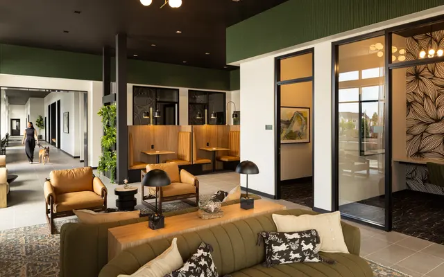 Stylish Modern Lobby Interior An open and modern lobby interior featuring a spacious seating area with a green couch and armchairs, decorative plants, and stylish lighting fixtures. The design includes booths for seating, large windows providing natural light, and artwork on the walls.