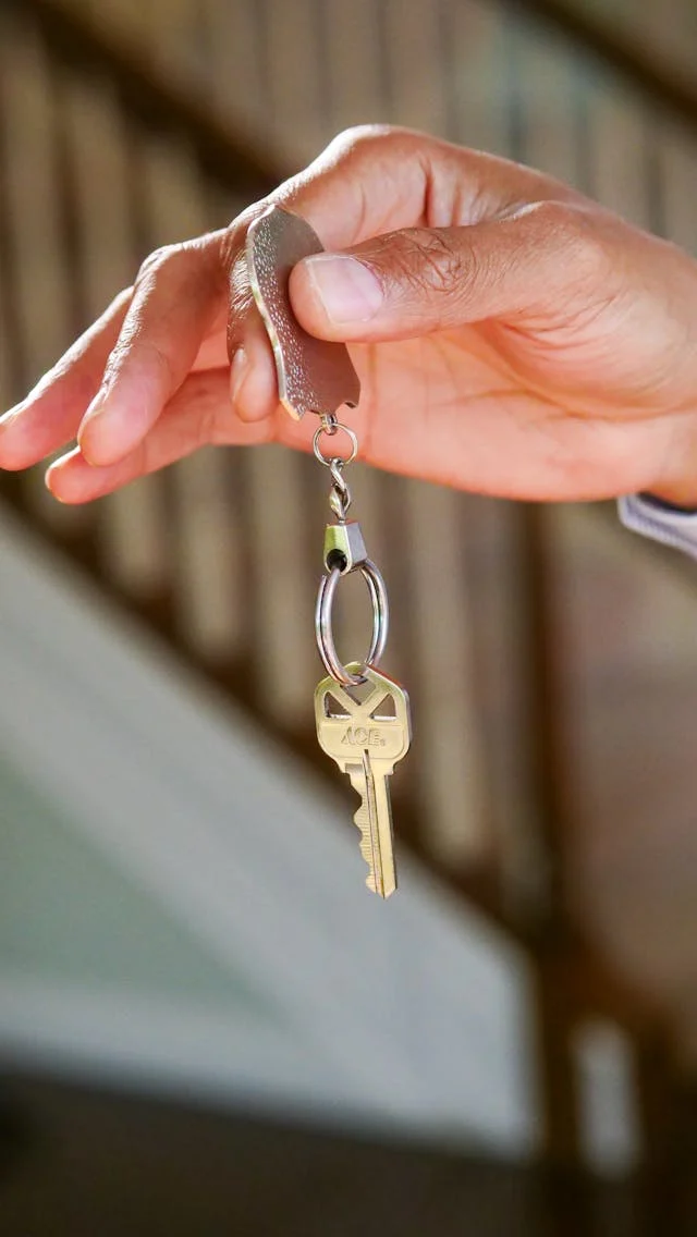 Holding a Key A hand holding a key attached to a metal keyring, with a staircase in the background.