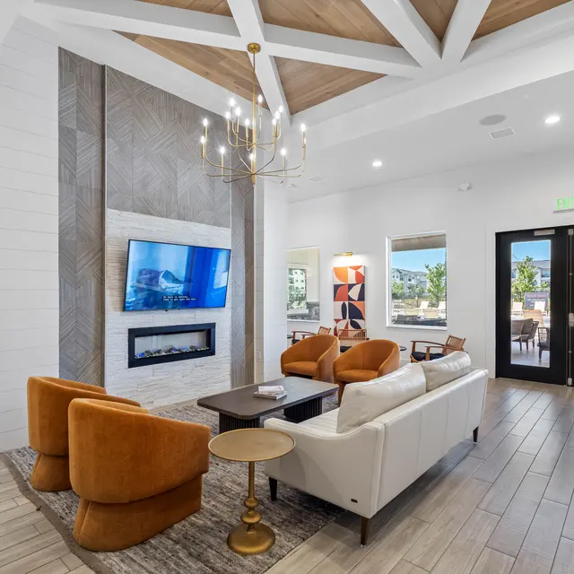 Stylish Modern Living Room A stylish modern living room featuring a fireplace, a large TV mounted on the wall, a white sofa, and orange armchairs. There is a round side table and large windows that allow natural light to fill the space.