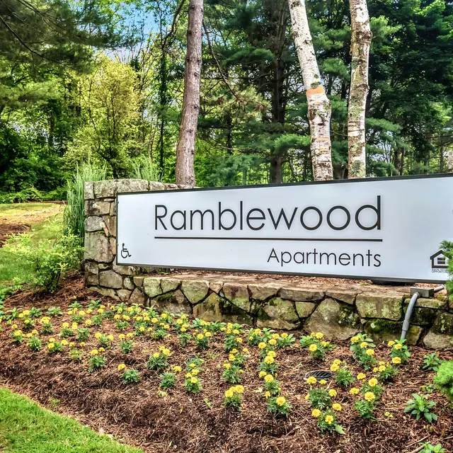 Sign for Ramblewood Apartments surrounded by greenery and flowers.
