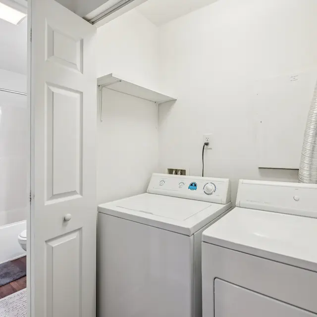 Laundry Room with Washer and Dryer A laundry room featuring a washing machine and dryer side by side, with a bathtub visible in the background.