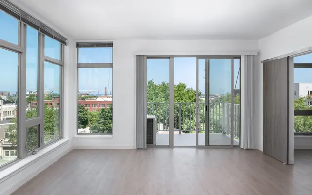 Empty room with hardwood floor, large windows, and balcony access with urban view.