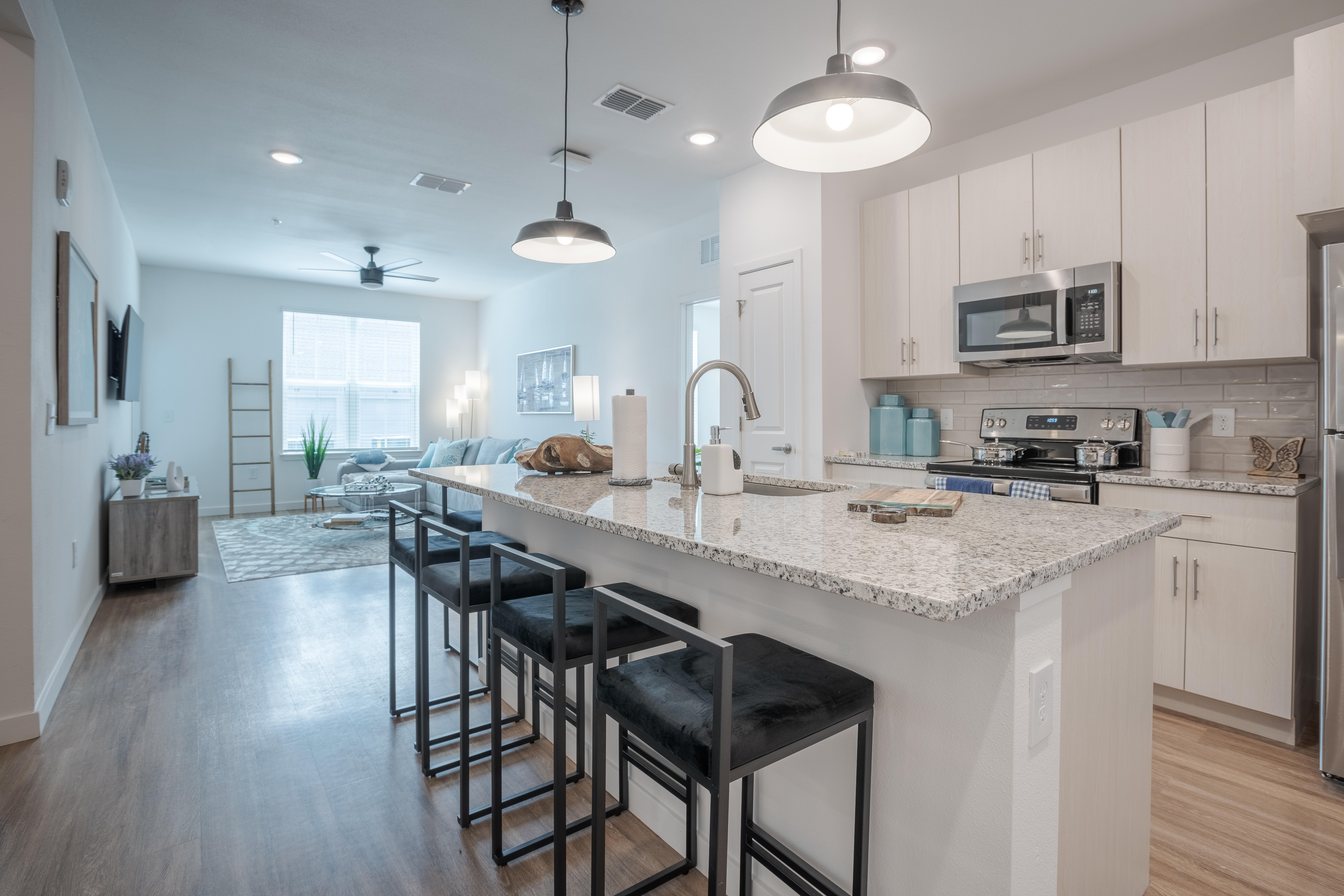 Enclave at Ayers-POI-010.jpg Modern kitchen with granite countertops, bar seating, and stainless steel appliances, leading to a bright living area.