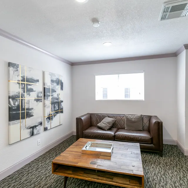 A modern living room featuring a brown leather couch, a wooden coffee table, and abstract artwork on the wall.