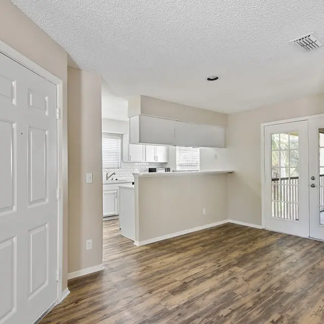 Venice Park living area on hardwood-style flooring with a door leading to a balcony, nestles next to a kitchen.