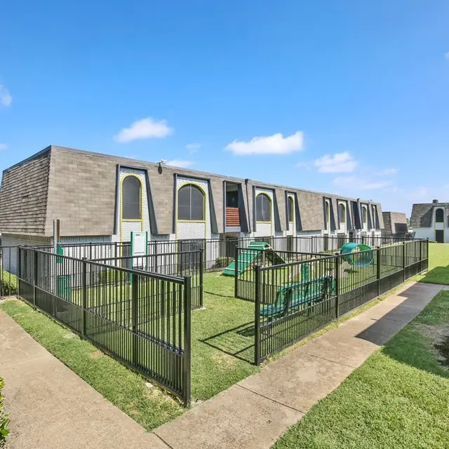 View of a modern apartment complex with a fenced area and green grass