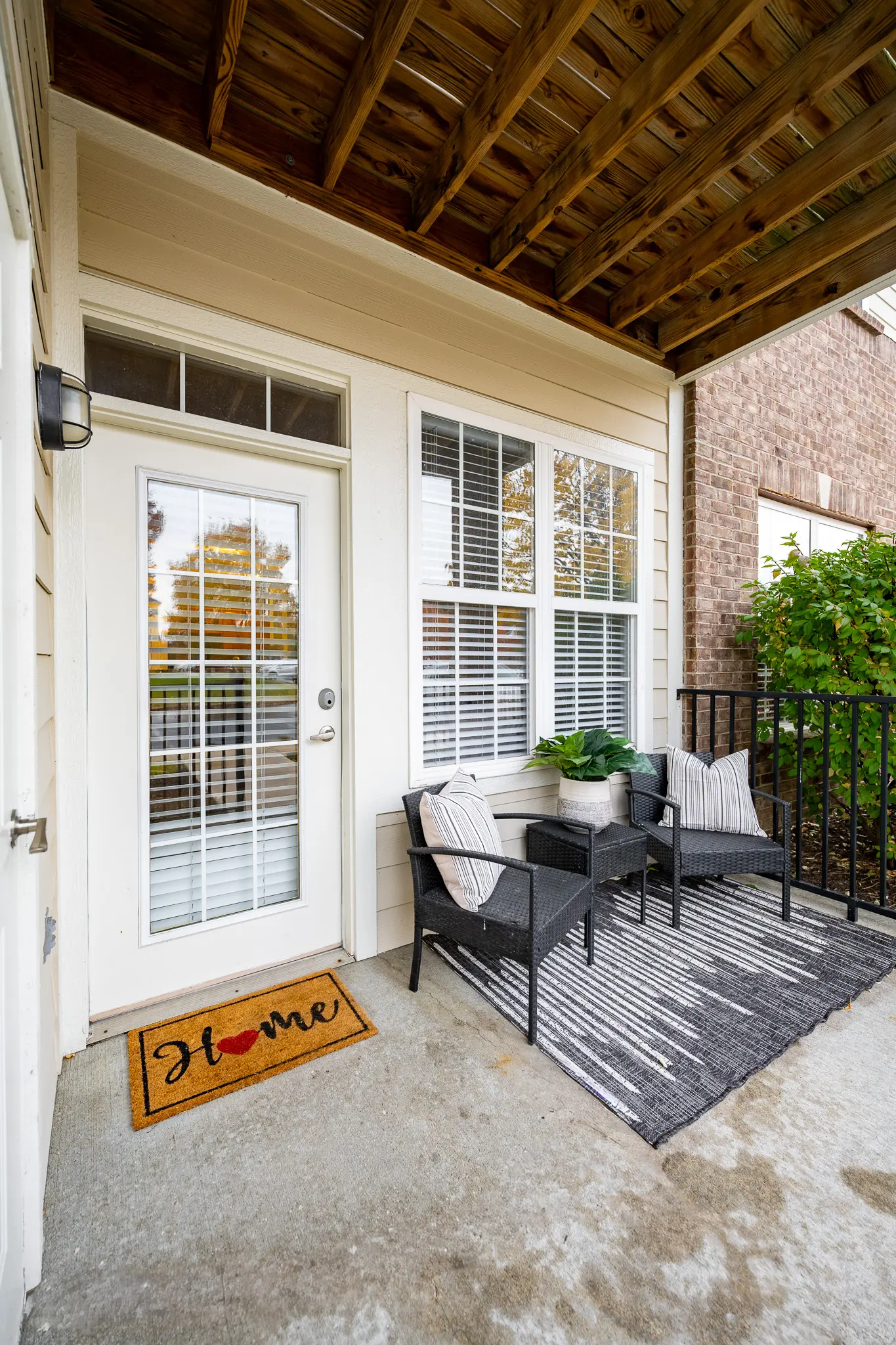 A cozy home entryway featuring a doormat that says 'Home', two chairs, a small table, and a potted plant. The entrance is well-lit by natural light and has a welcoming vibe.