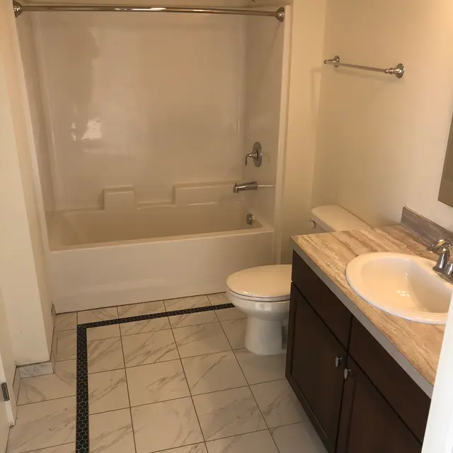 Modern Bathroom Interior A clean and simple bathroom featuring a bathtub with a shower, a toilet, and a vanity with a sink. The floor is tiled, and the wall colors are light.