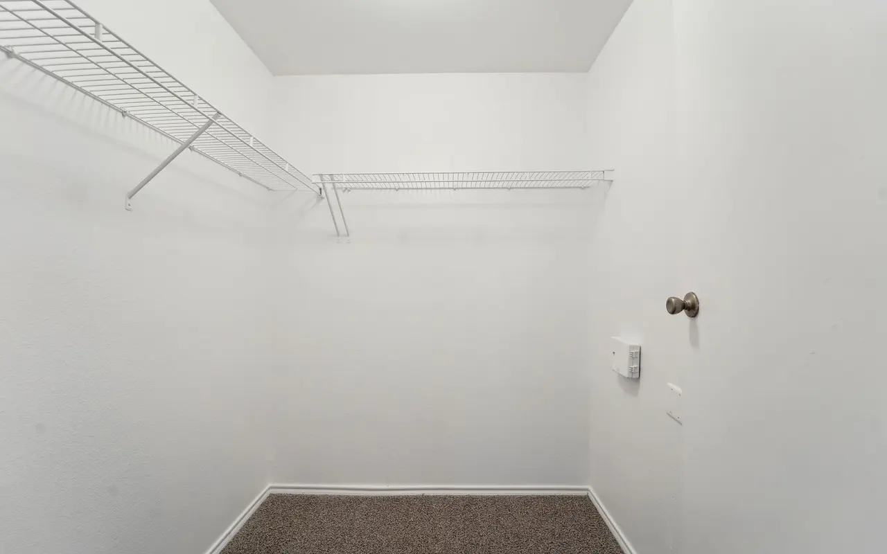 An empty walk-in closet with white walls, a carpeted floor, and wire shelving on one side.