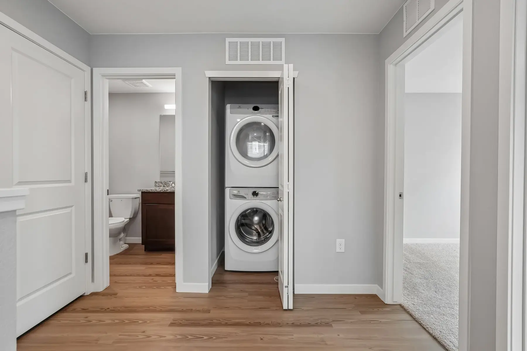 Compact Laundry Area in Hallway A small hallway featuring a stacked washer and dryer, with doors leading to a bathroom and another room.
