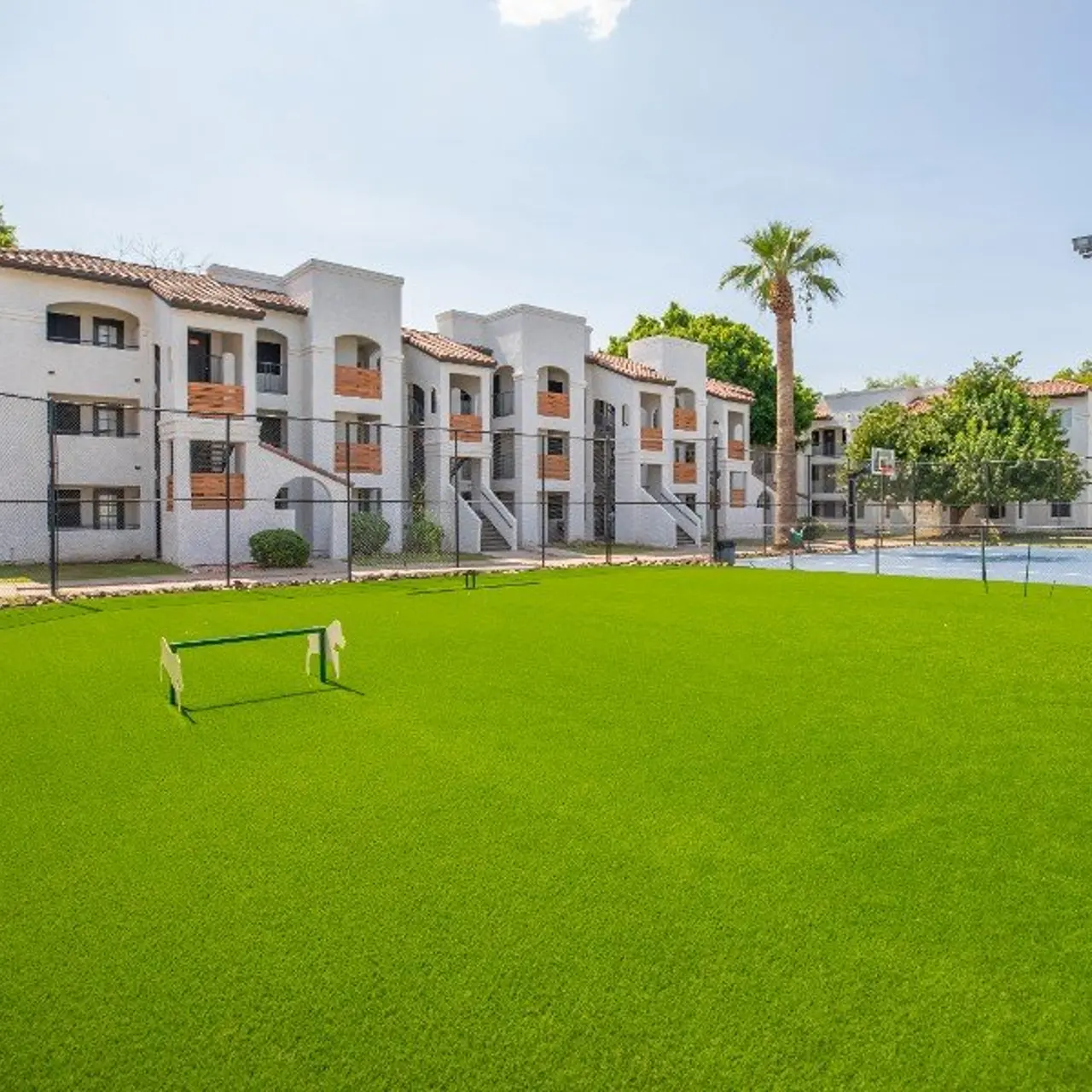 View of an apartment complex next to a green lawn and tennis court.