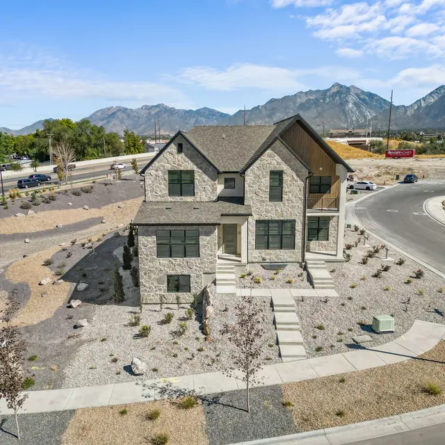 A modern stone house with a triangular roof surrounded by gravel landscaping and mountains in the background.