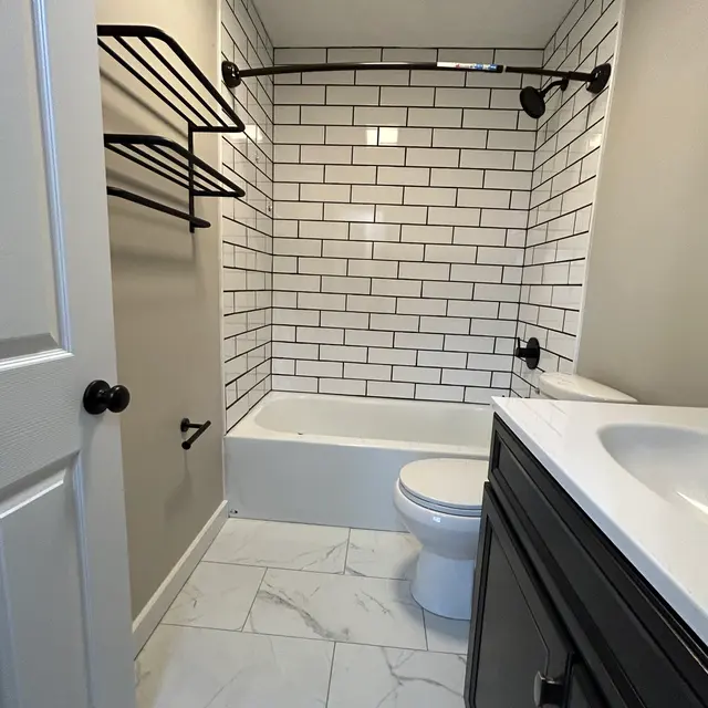 A modern bathroom featuring a bathtub with white subway tile walls, a black towel rack, and a dark cabinet under the sink against a neutral wall.