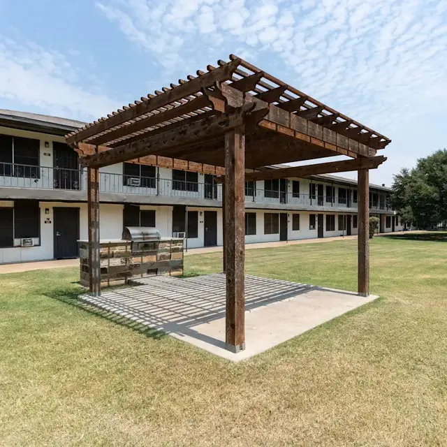 Pergola at Apartment Complex An outdoor pergola structure in front of a two-story apartment complex with grassy areas.