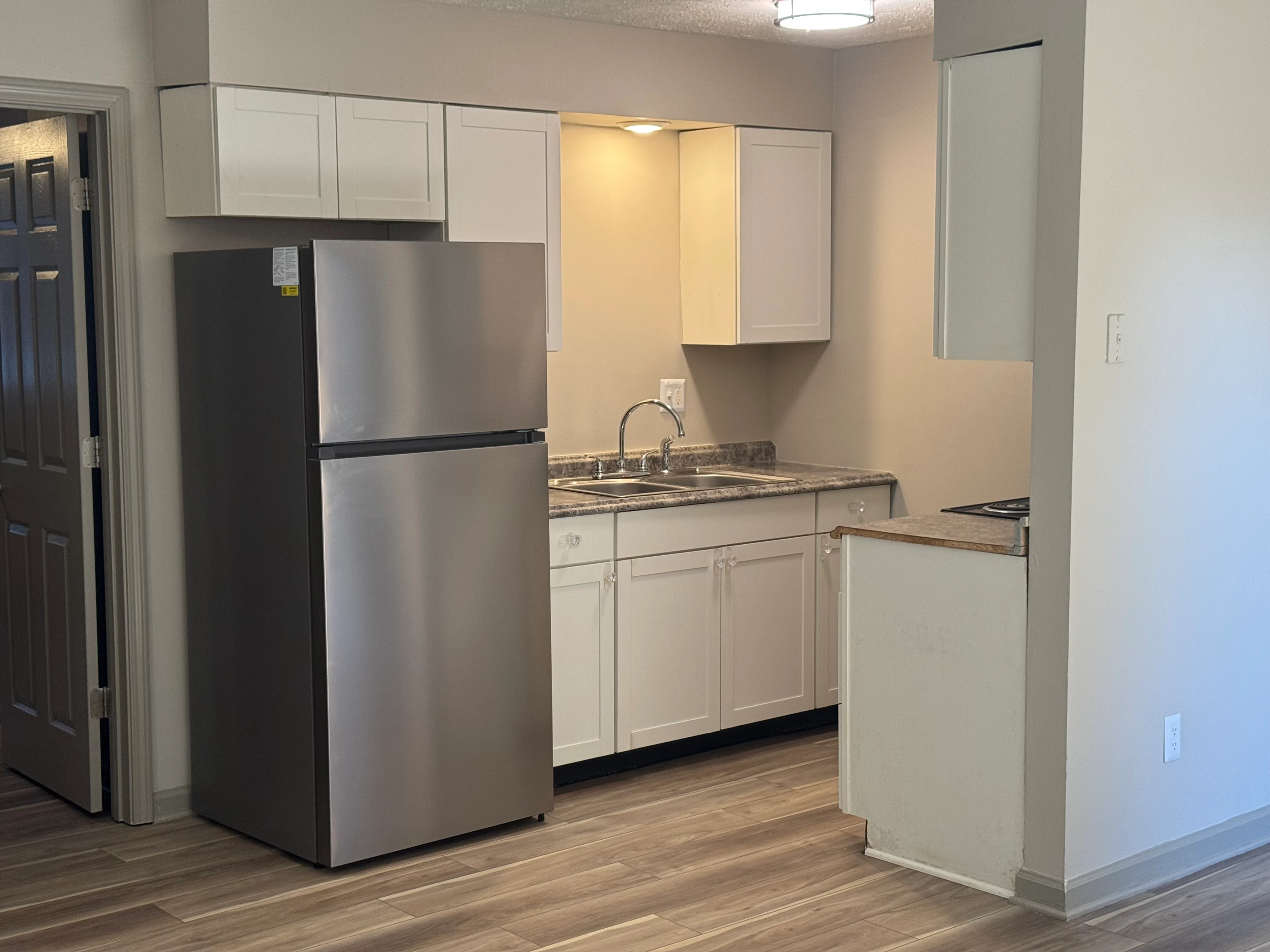 Modern Kitchen Interior A modern kitchen featuring a silver refrigerator, white cabinets, a countertop with a sink, and wooden flooring. The walls are painted in a light color, and there is an open layout leading to another room.