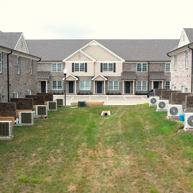 View of an apartment complex courtyard featuring several air conditioning units on the ground and grass in between two rows of buildings.