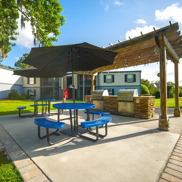 Outdoor communal grilling area with a covered pergola, picnic tables, and barbecue grills.