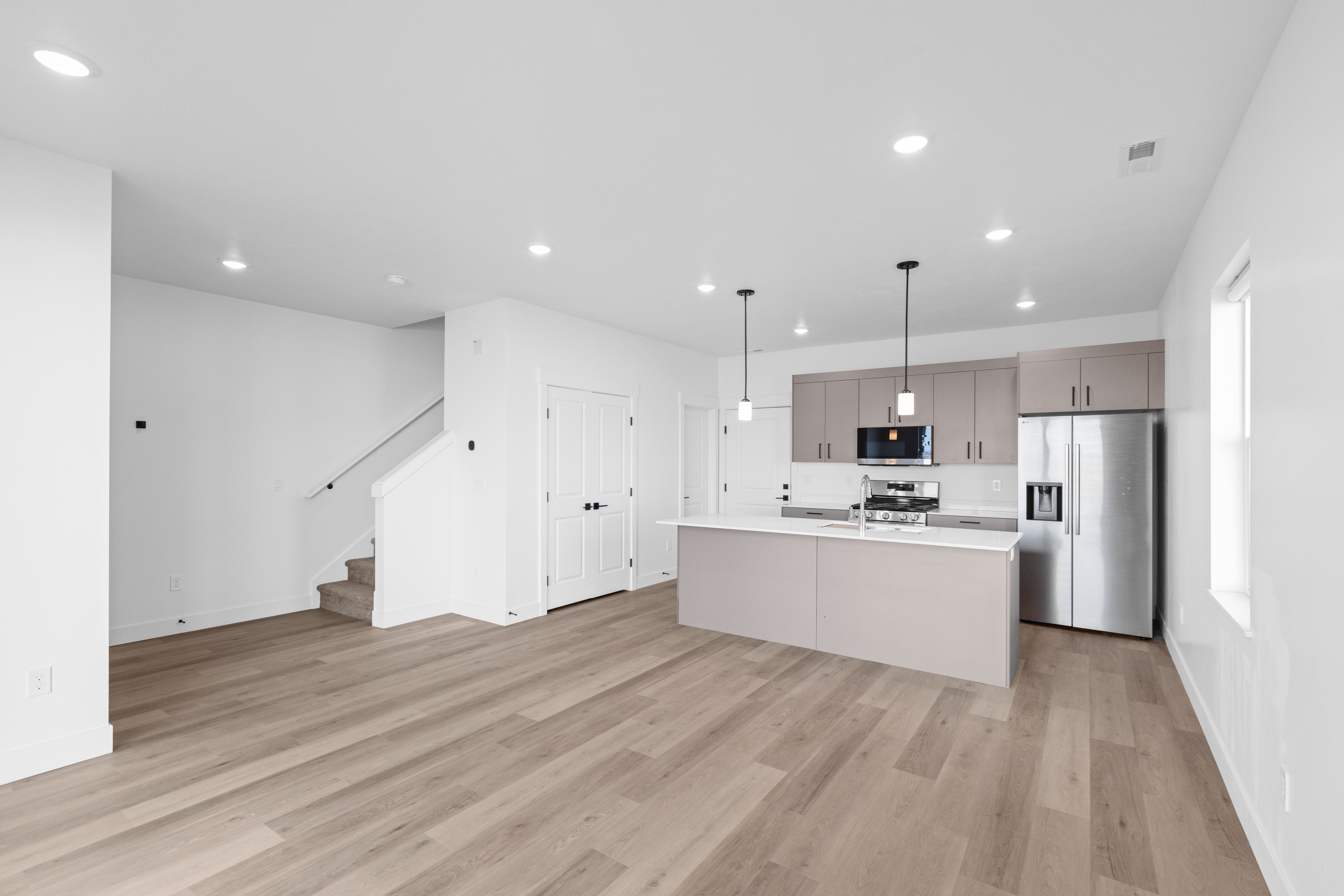 Contemporary Apartment Interior A modern apartment kitchen and living area featuring an open layout with wooden flooring, white walls, and a kitchen island with a contemporary design. The kitchen is equipped with stainless steel appliances and has pendant lighting above the island. A staircase is visible in the background leading to another level.