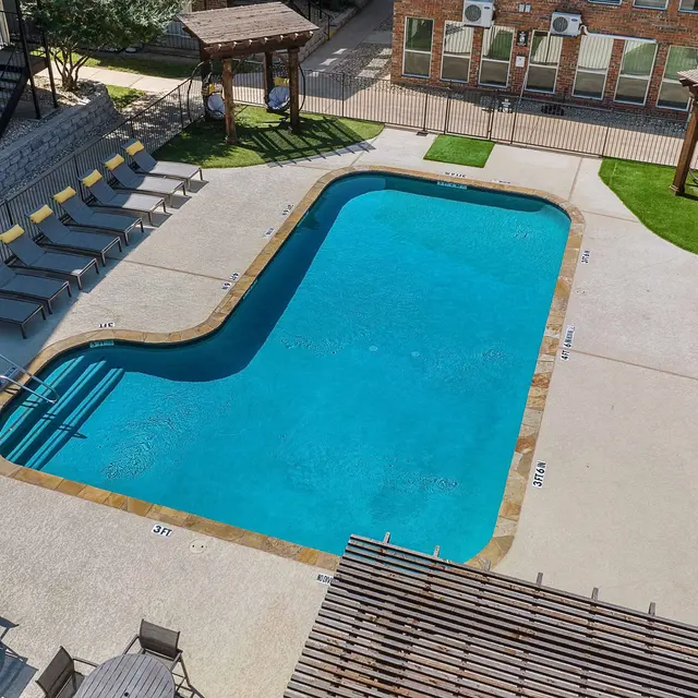 Aerial view of a swimming pool at an apartment complex with lounge chairs and shade structures.