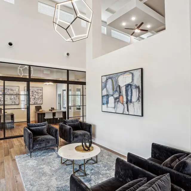 Modern lobby with dark velvet chairs, a circular coffee table, framed artwork, and large windows, creating a bright and inviting space.