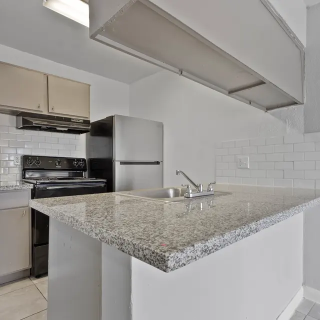 A modern kitchen featuring a granite countertop, black appliances, white subway tile backsplash, and a fire extinguisher mounted on the wall.