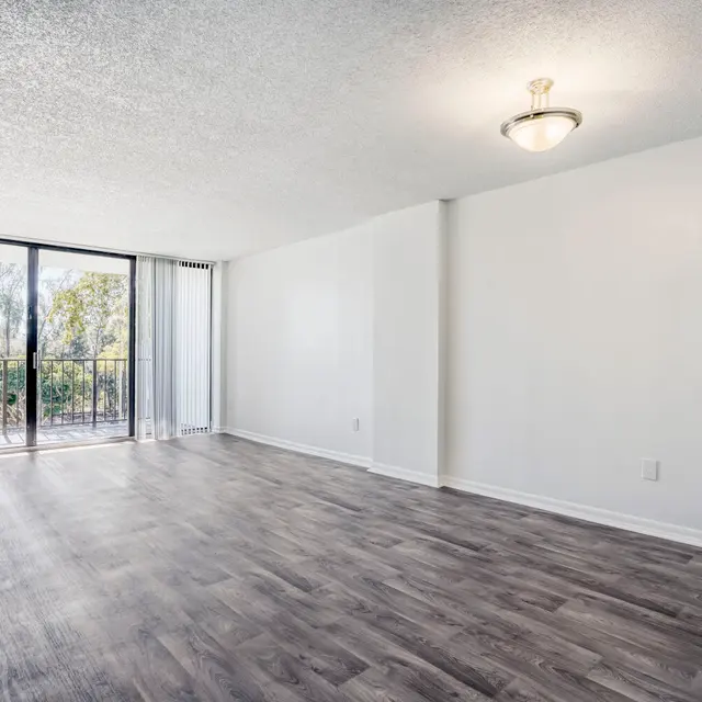 Bright and Spacious Empty Living Room An empty living room with large windows and a balcony, featuring a modern light fixture and grey wooden flooring.
