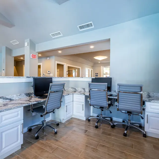 Modern Workspace Design A modern workspace with a light blue wall, featuring a granite countertop and several office chairs against it. In the background, kitchen-style features are visible, along with a window allowing natural light inside.