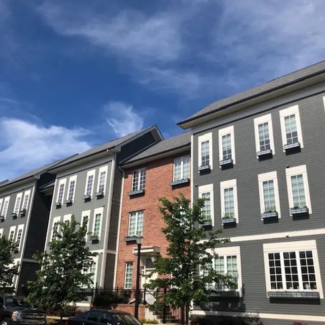 Modern Apartment Buildings Under Clear Blue Sky A view of modern apartment buildings featuring a mix of brick and gray siding, with trees at the base and a clear blue sky above.