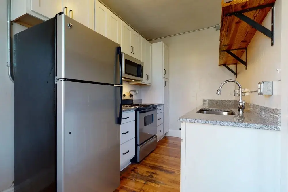 A compact kitchen featuring stainless steel appliances, including a refrigerator, stove, and microwave. There are white cabinets and a countertop with a sink.