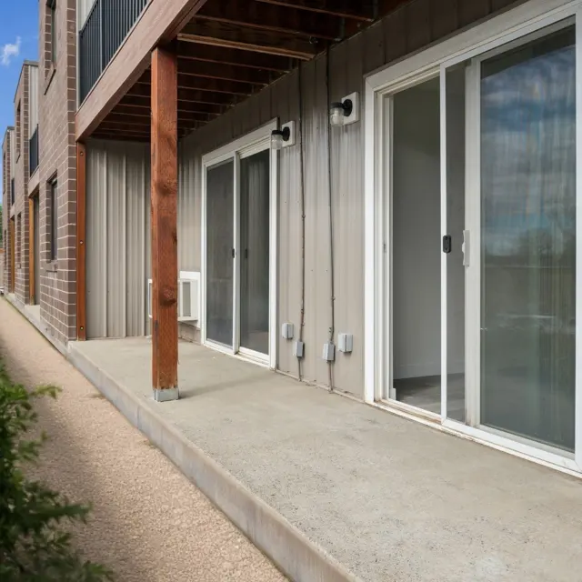 Modern Apartment Exterior Exterior view of an apartment complex with concrete patio, sliding glass doors, and greenery alongside a stone pathway.