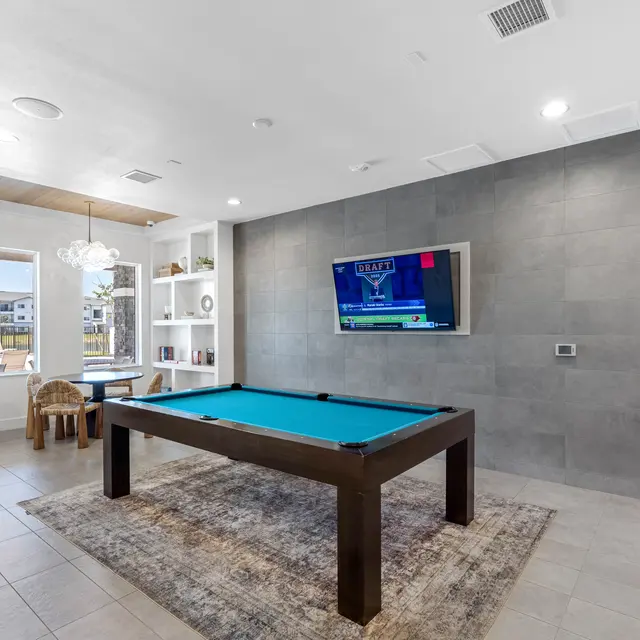Modern Game Room with Pool Table A modern game room featuring a turquoise pool table, gray tiled walls, a television mounted on the wall, and a cozy seating area with a round table and chairs.