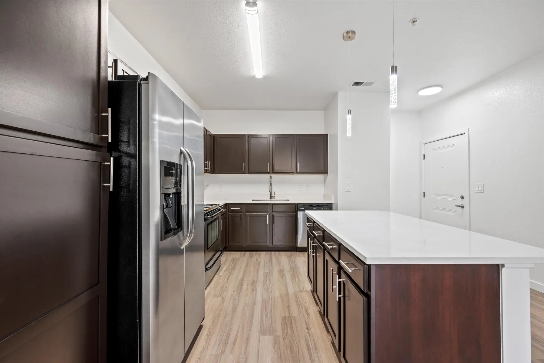 A modern kitchen with stainless steel appliances, dark cabinetry, and a large island with a white countertop.