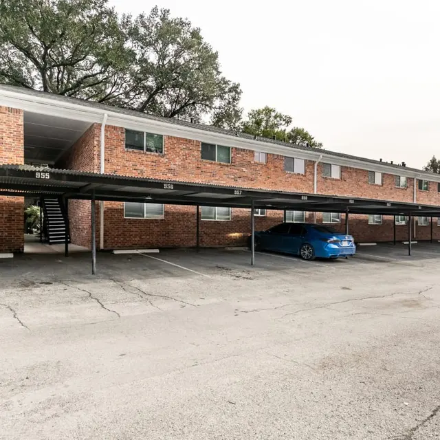Exterior view of a brick apartment complex with covered parking spaces.