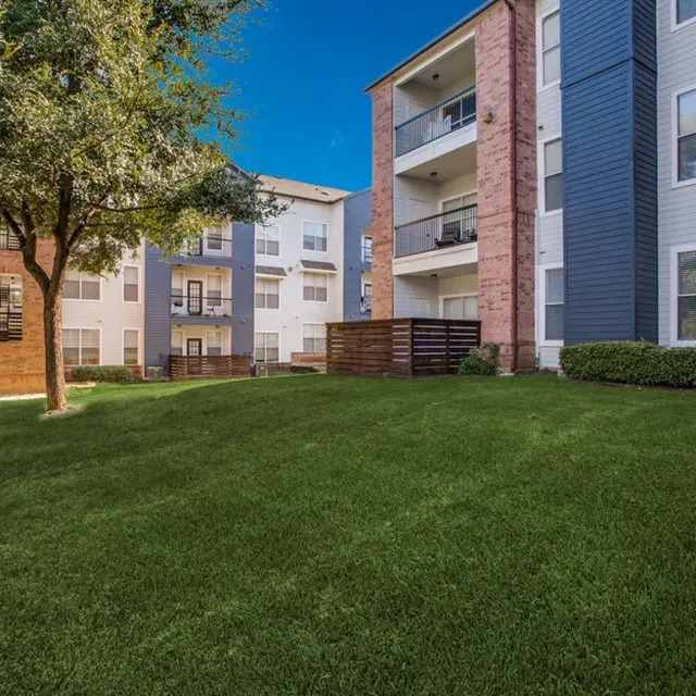 A view of modern apartment buildings with a green lawn and trees in the foreground.
