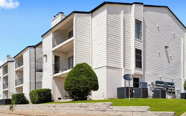 A modern apartment building with multiple levels, featuring a white exterior, balconies, and manicured lawns.