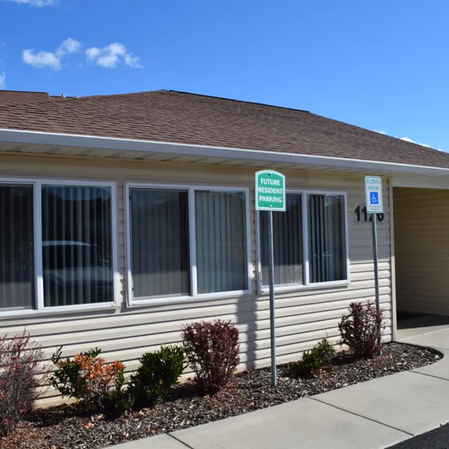 Exterior of a Single-Story Building A single-story building with large windows, a flat roof, and a path leading to the entrance. A sign indicating future parking is visible. The surroundings include shrubs and a clear blue sky.