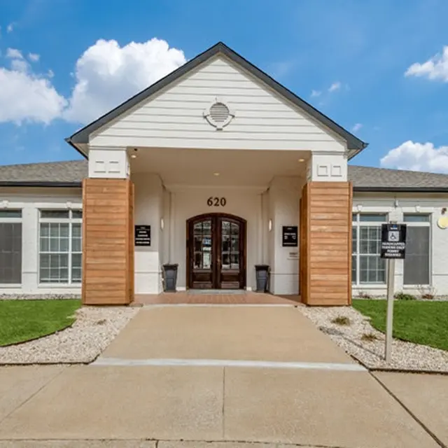 Exterior view of a modern community center with a welcoming entrance and landscaped lawn under a blue sky with fluffy clouds.