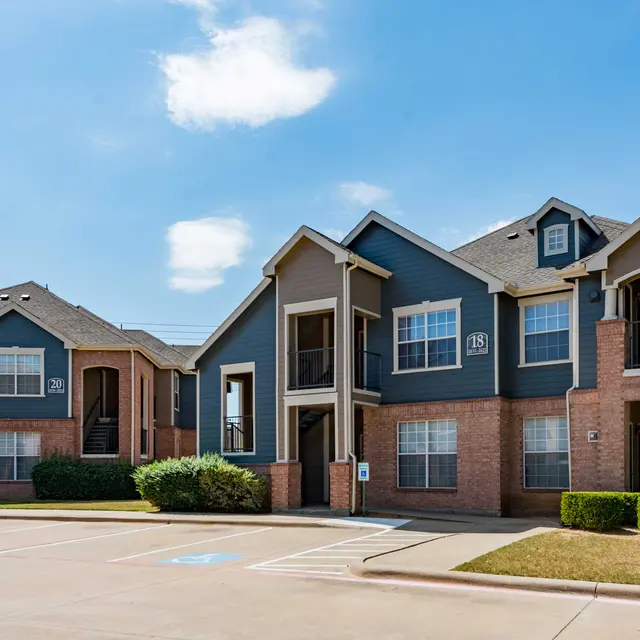A modern two-story apartment complex featuring brick exteriors and light blue accents under a clear sky.