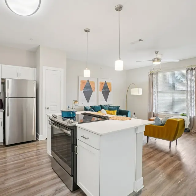 A modern kitchen features white cabinets and stainless steel appliances, with an open layout leading to a cozy living room area decorated with colorful furniture.
