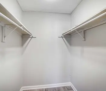 An empty closet with two hanging rods on either side and light gray walls.